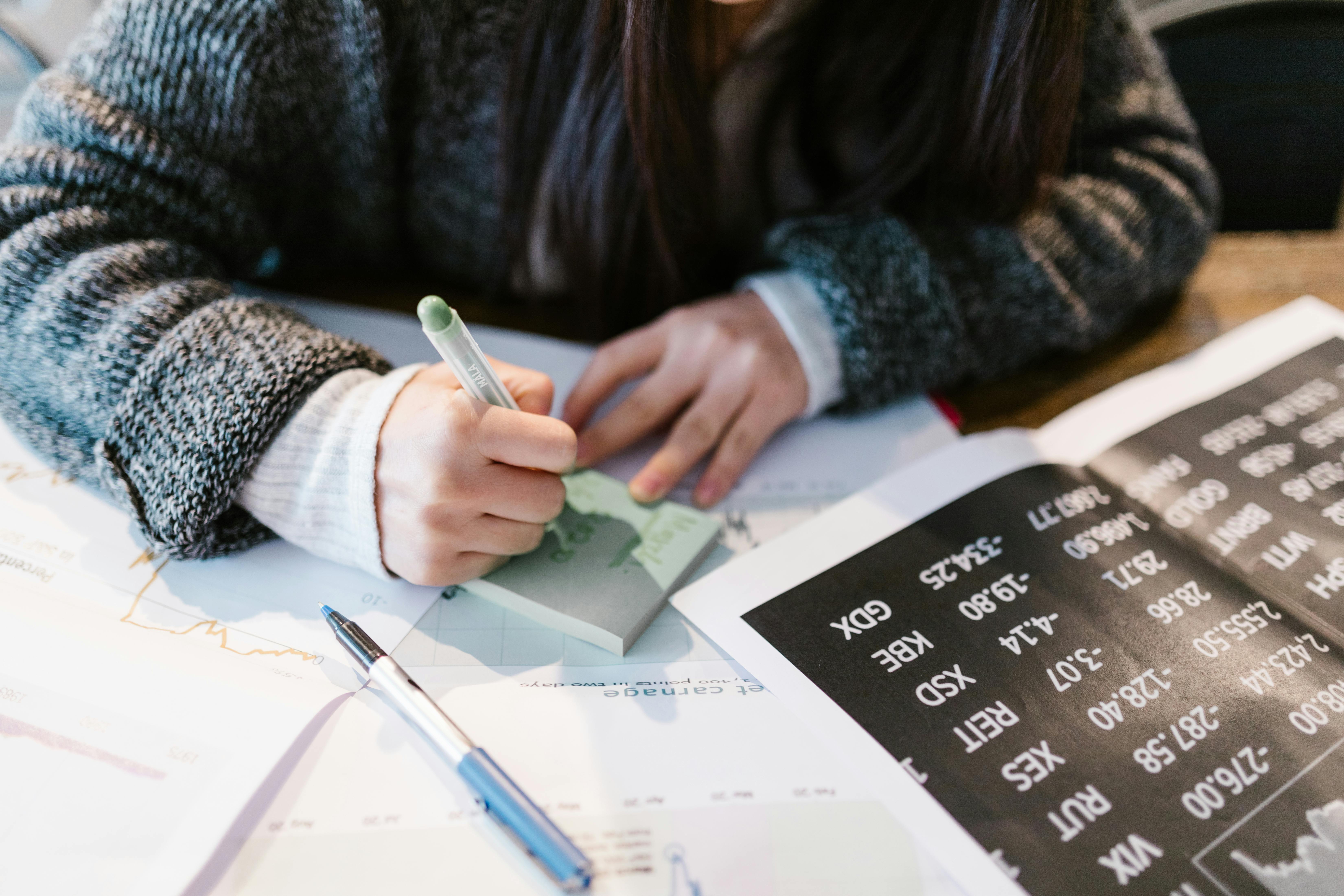 woman in gray sweater holding pen writing on white paper