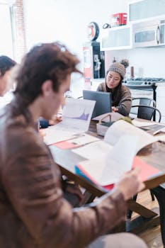 Focused coworkers collaborate around a table with laptops and documents in a stylish office.