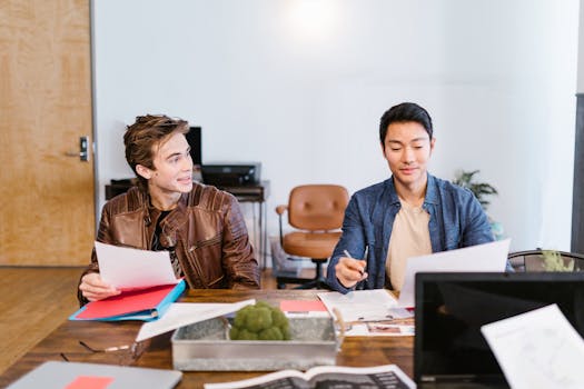 Two colleagues discussing work in a modern office setting, focused on documents.