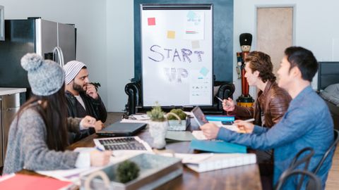 Equipo diverso trabajando alrededor de una mesa en una oficina startup, planificando y discutiendo ideas