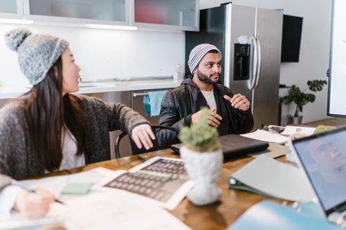 Free Two coworkers having a discussion in a contemporary office setting, surrounded by office supplies and technology. Stock Photo