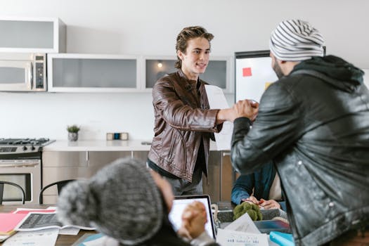 Two young men shaking hands in a modern office setting, symbolizing teamwork.