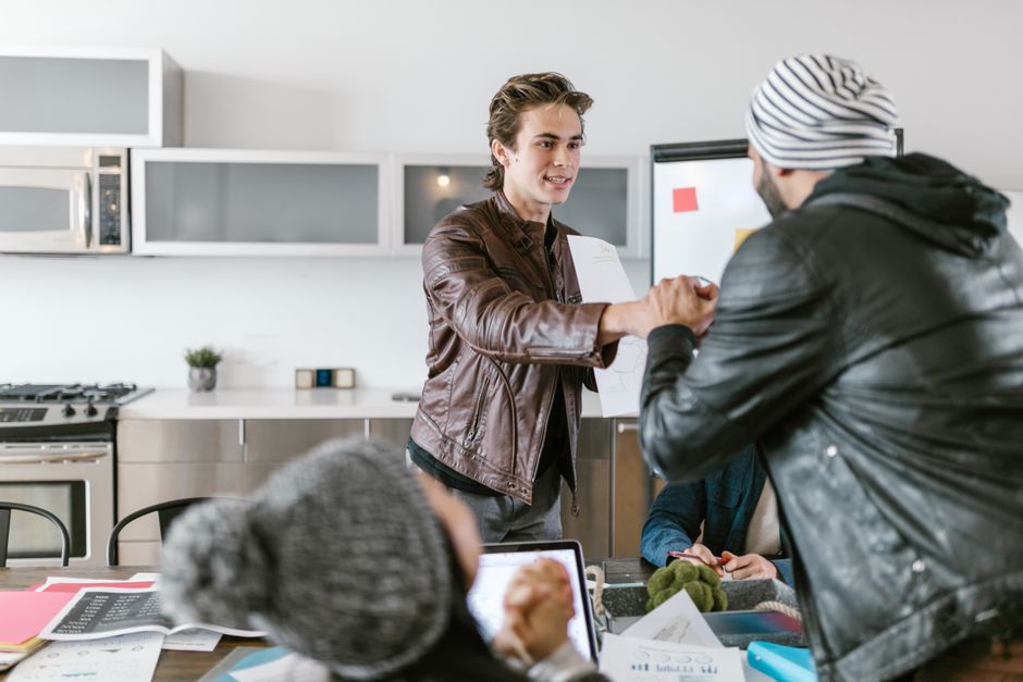 Two young men shaking hands in a modern office setting, symbolizing teamwork. Two young men shaking hands in a modern office setting, symbolizing teamwork.