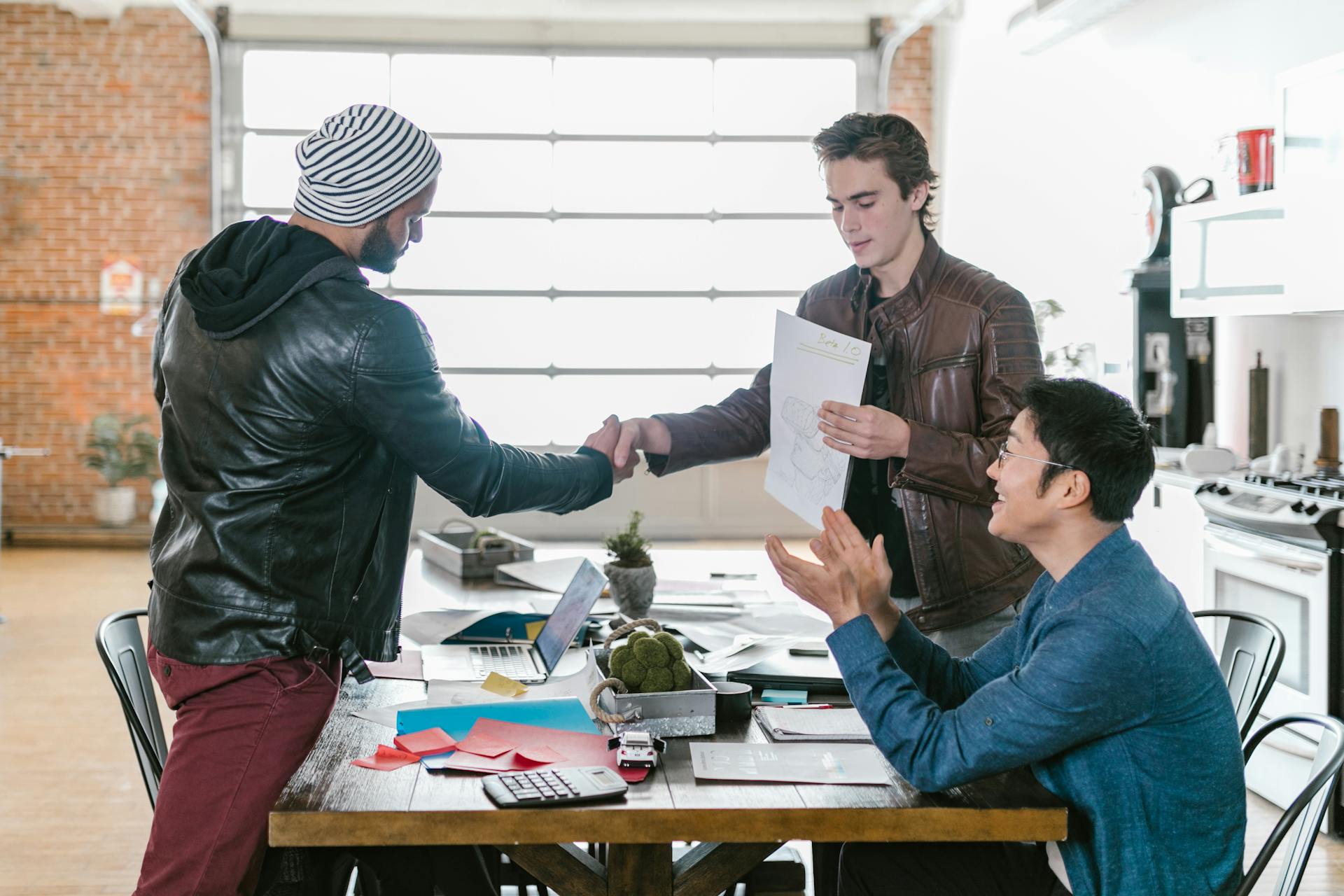 Three entrepreneurs collaborate and shake hands in a modern office setting, showcasing teamwork and agreement.