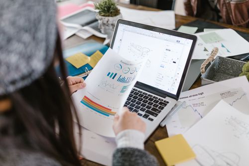 Free A person reviewing printed graphs with a laptop in a modern workspace. Stock Photo