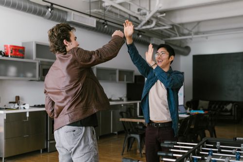 Free Two male friends happily high fiving in a modern office setting, displaying friendship and positivity. Stock Photo