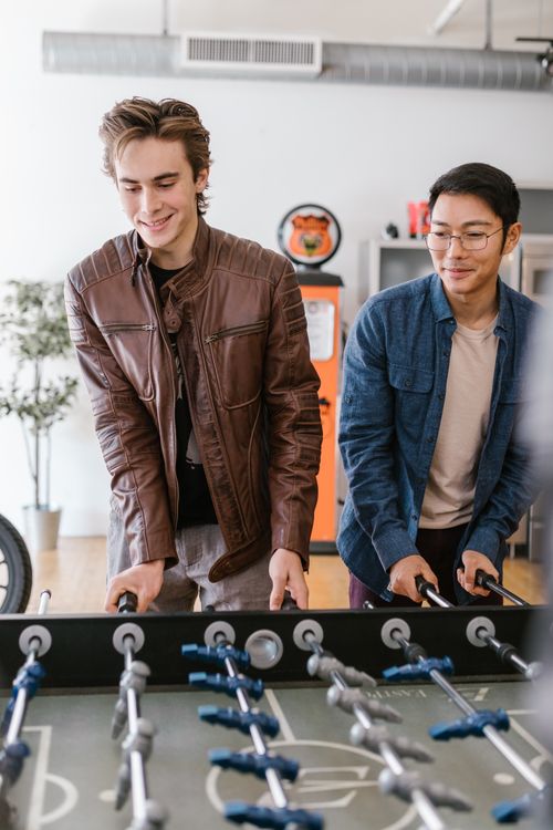 Free Two friends have fun playing foosball in a cozy indoor setting, showcasing joy and friendship. Stock Photo