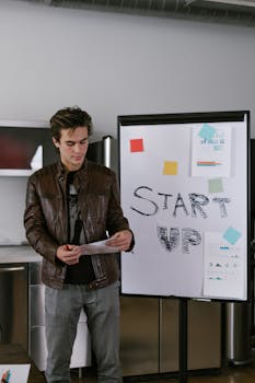 Young man in a brown leather jacket presenting startup ideas on a flip chart.