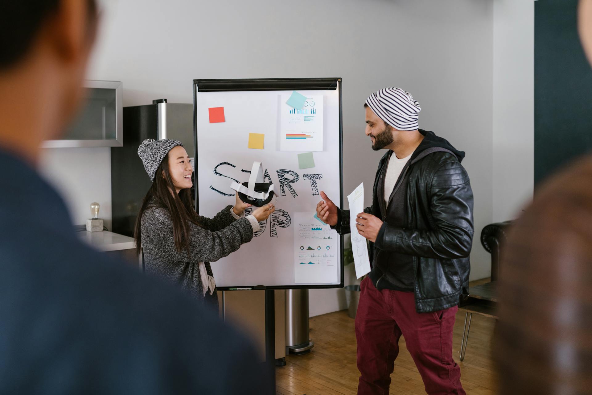 A diverse group of coworkers brainstorming in a modern startup environment, presenting ideas on a whiteboard.