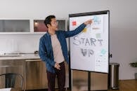 Man in Blue Shirt Pointing at Paper on White Board