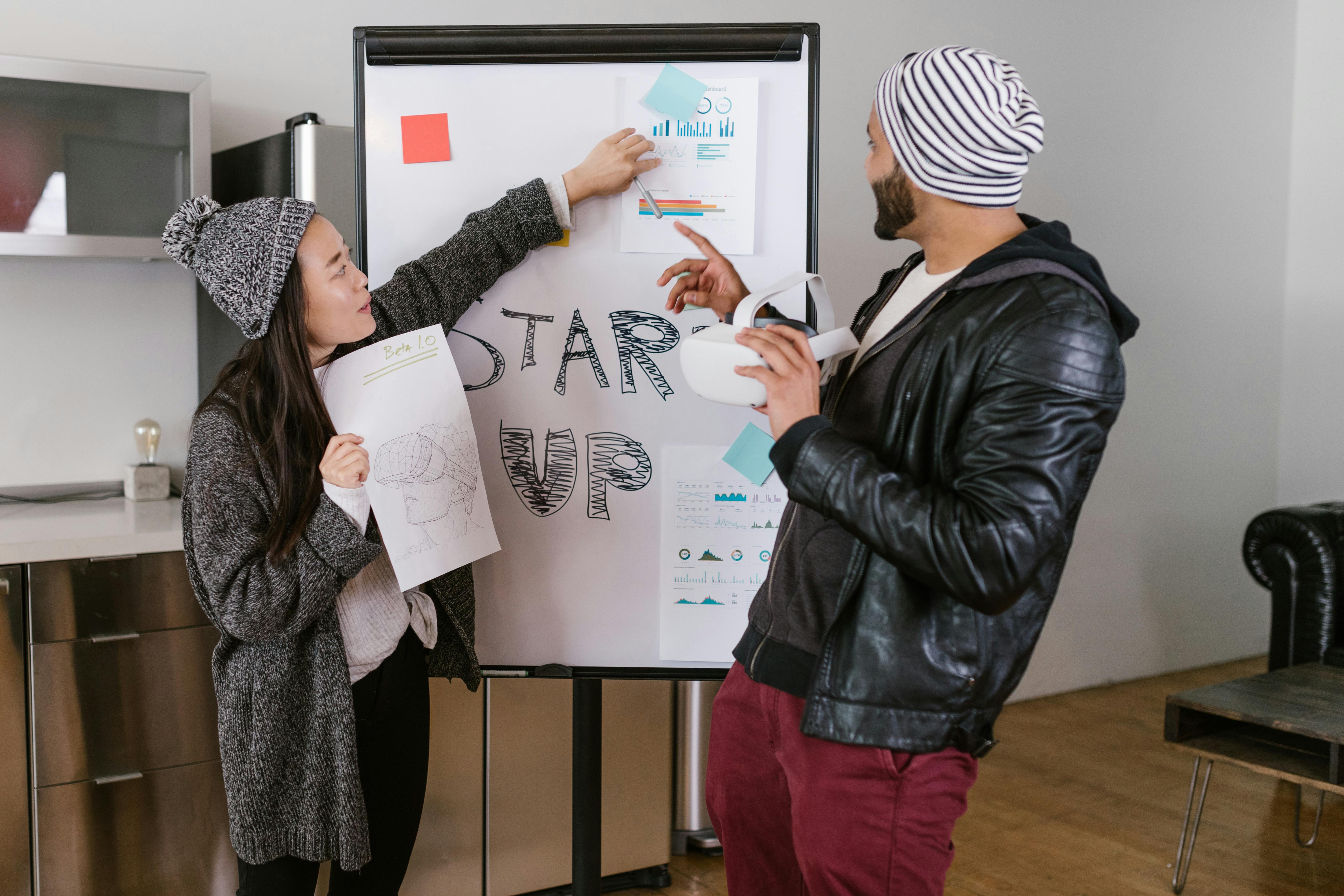 Two young adults presenting startup business ideas on a flipchart indoors.