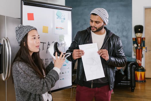 Asian woman and Indian man discussing ideas with whiteboard presentations in a coworking space.