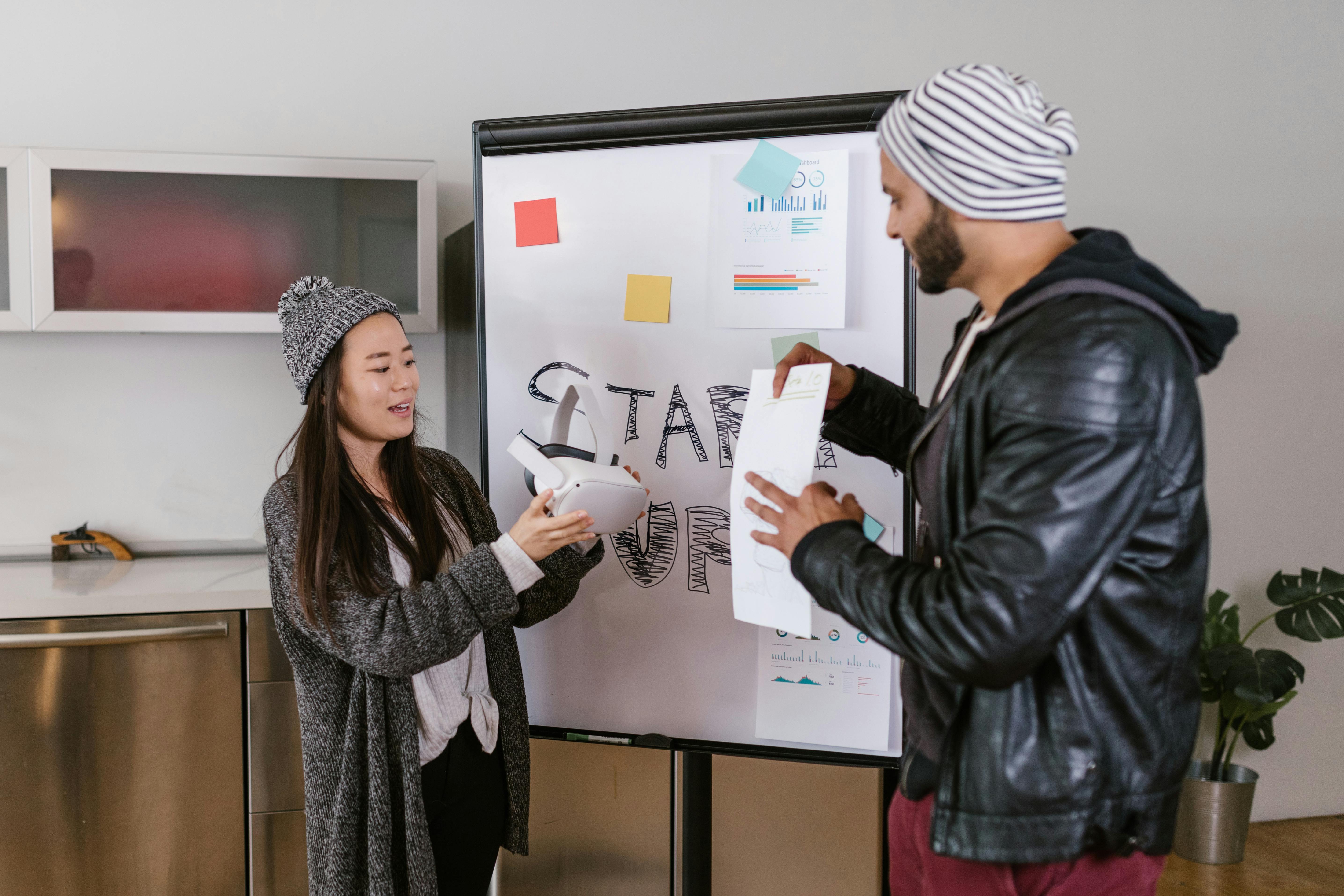 Two coworkers collaborate on a startup presentation using a whiteboard indoors.