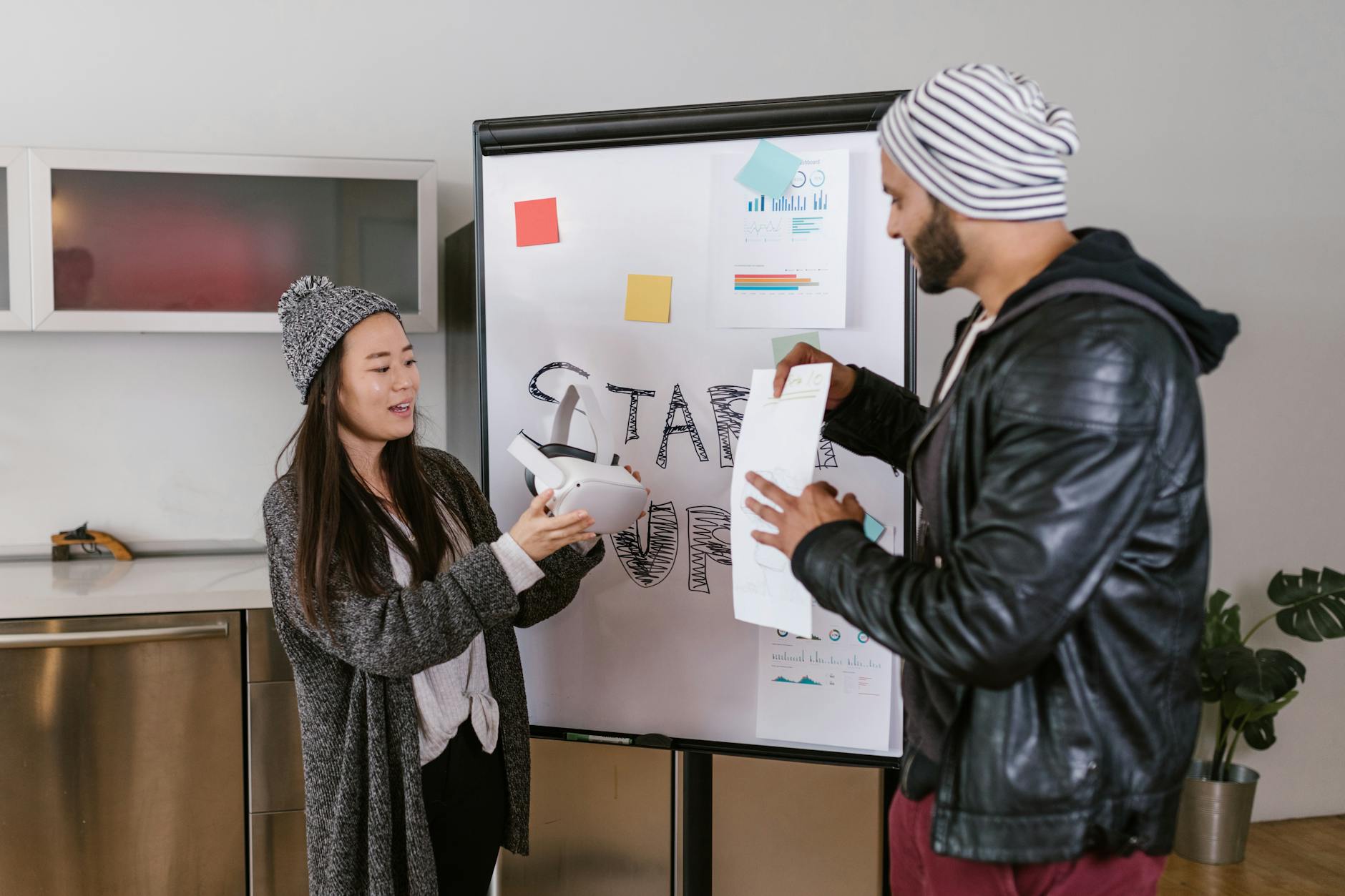 Two coworkers collaborate on a startup presentation using a whiteboard indoors.