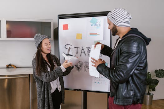 Two coworkers collaborate on a startup presentation using a whiteboard indoors.