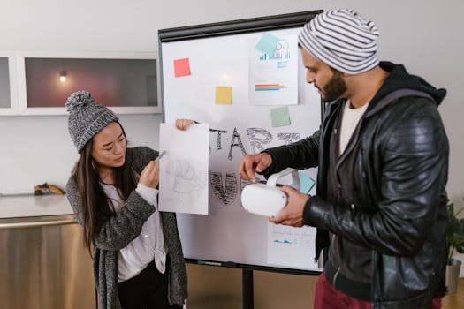 Two young coworkers discuss a project using sketches and VR headset inside a cozy office.