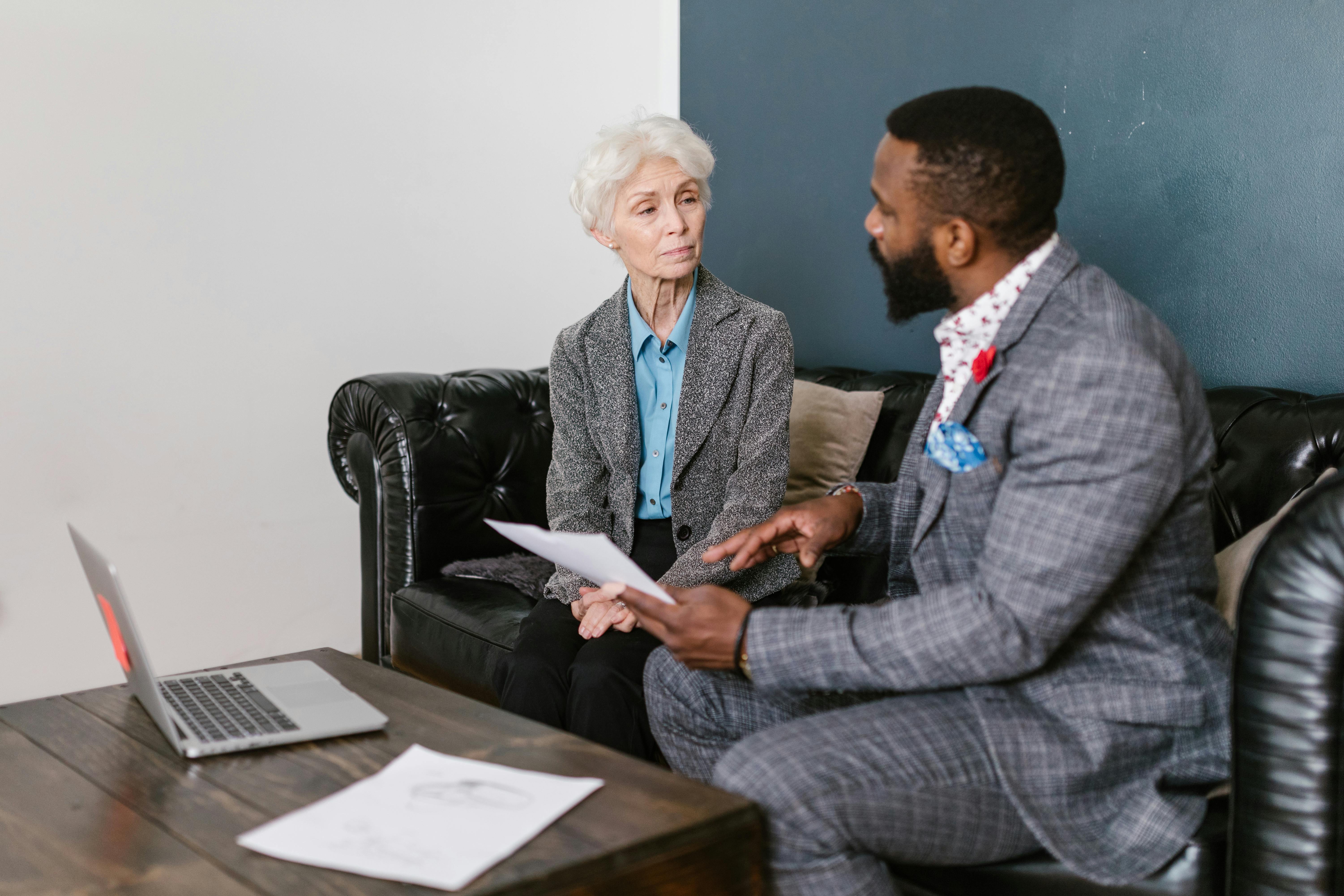 An elderly woman and a man in a professional meeting discussing documents indoors.