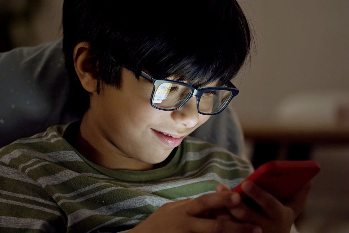 Free Boy Wearing Eyeglasses Using a Cellphone Stock Photo
