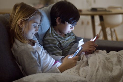 Free Kids Using Gadgets While on a Sofa Bed Stock Photo