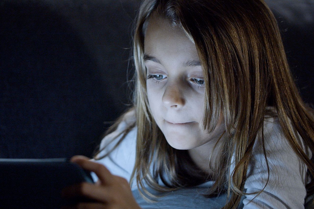 a young girl using a digital tablet in bed bathed in soft light focuse