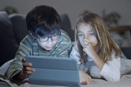 Free Two children engaging with a tablet indoors, creating a bonding moment. Cozy setting. Stock Photo