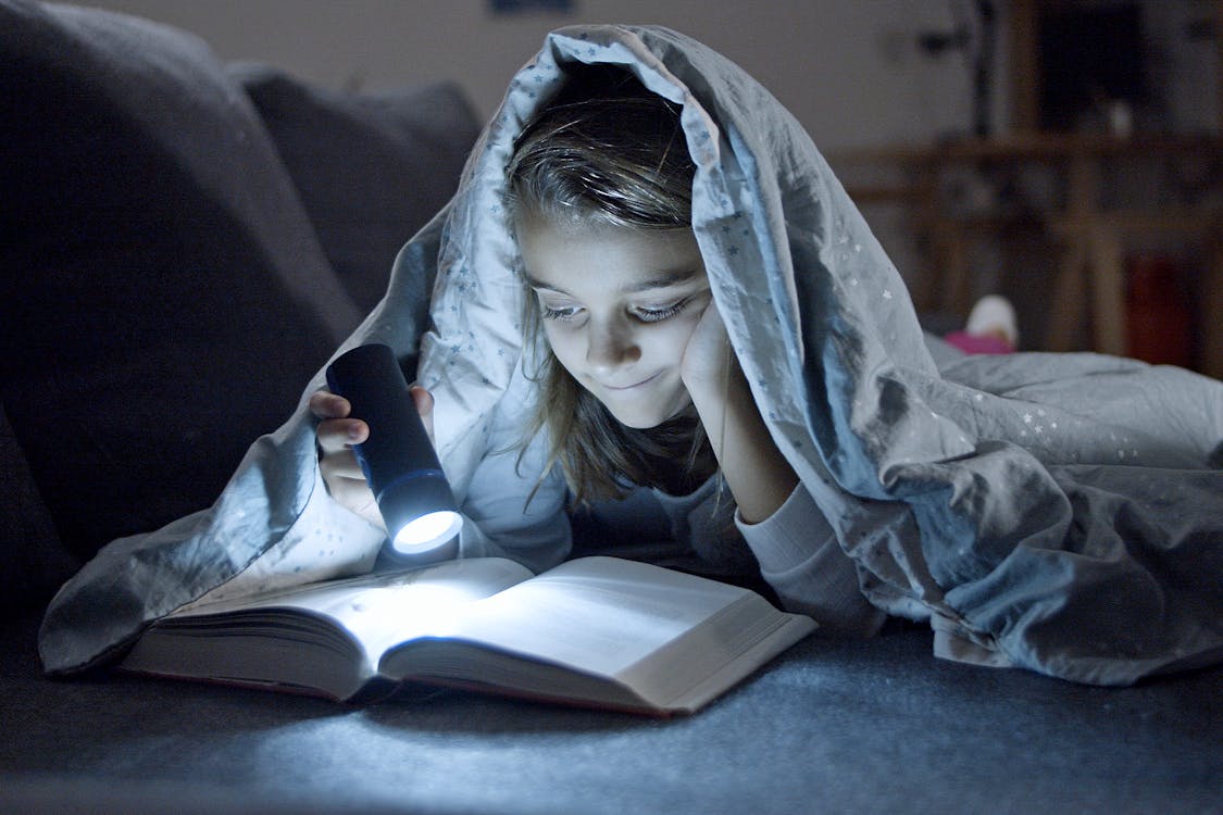 Kid reading in the dark with flashlight