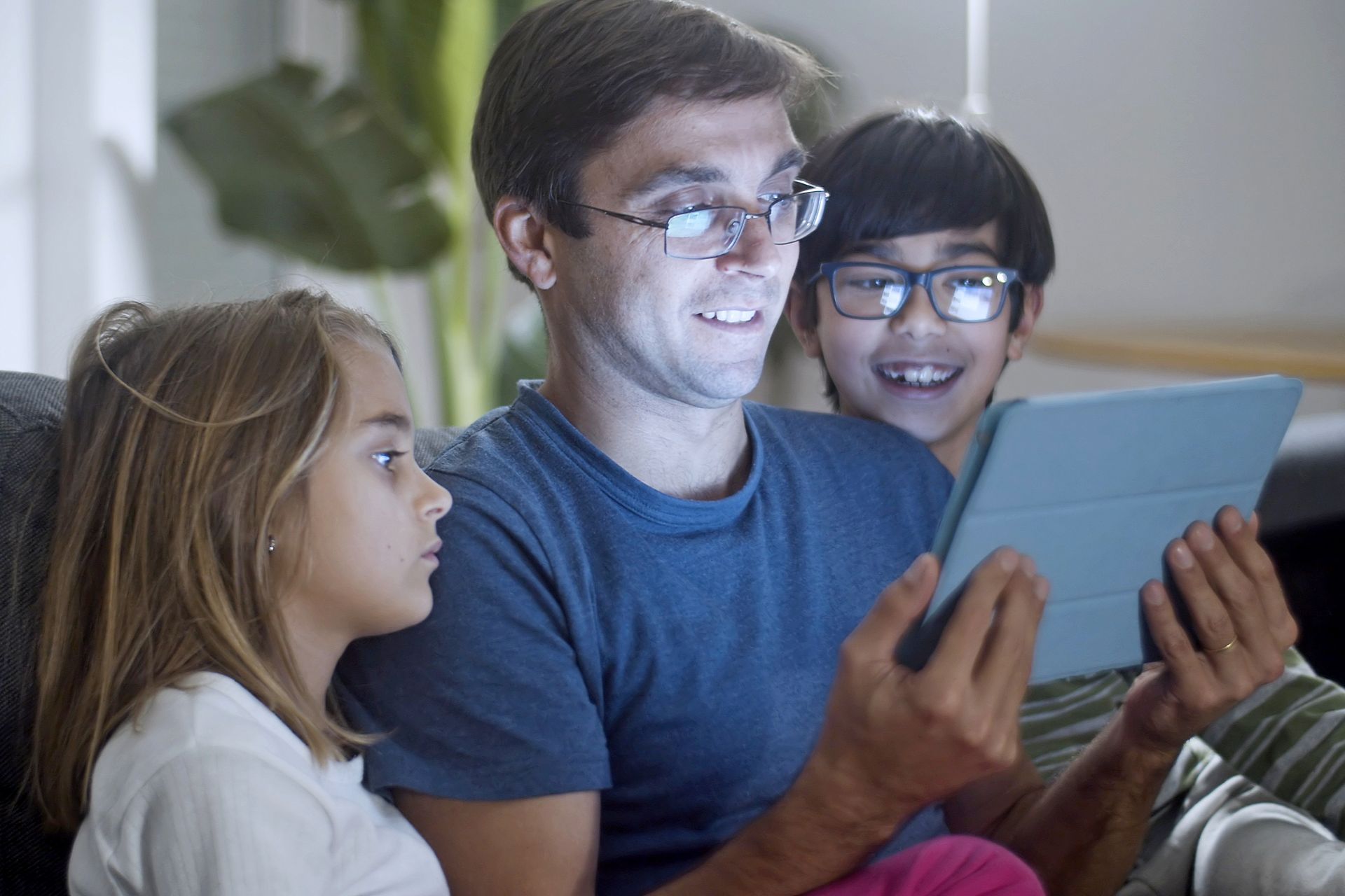 A father and children enjoying time together using a digital tablet at home.