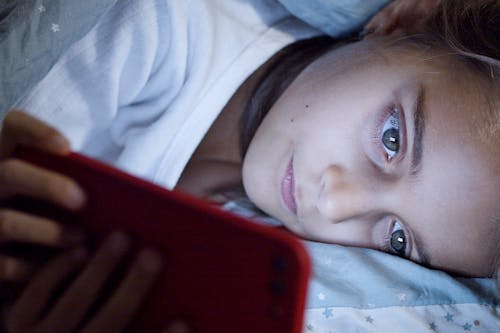Free Young Girl Lying While Using a Smartphone Stock Photo