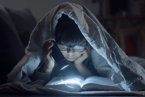 Free Kid Lying on a Bed While Reading a Book Stock Photo