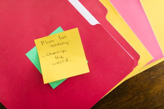 Yellow Post-it note with motivational text on colorful office folders.