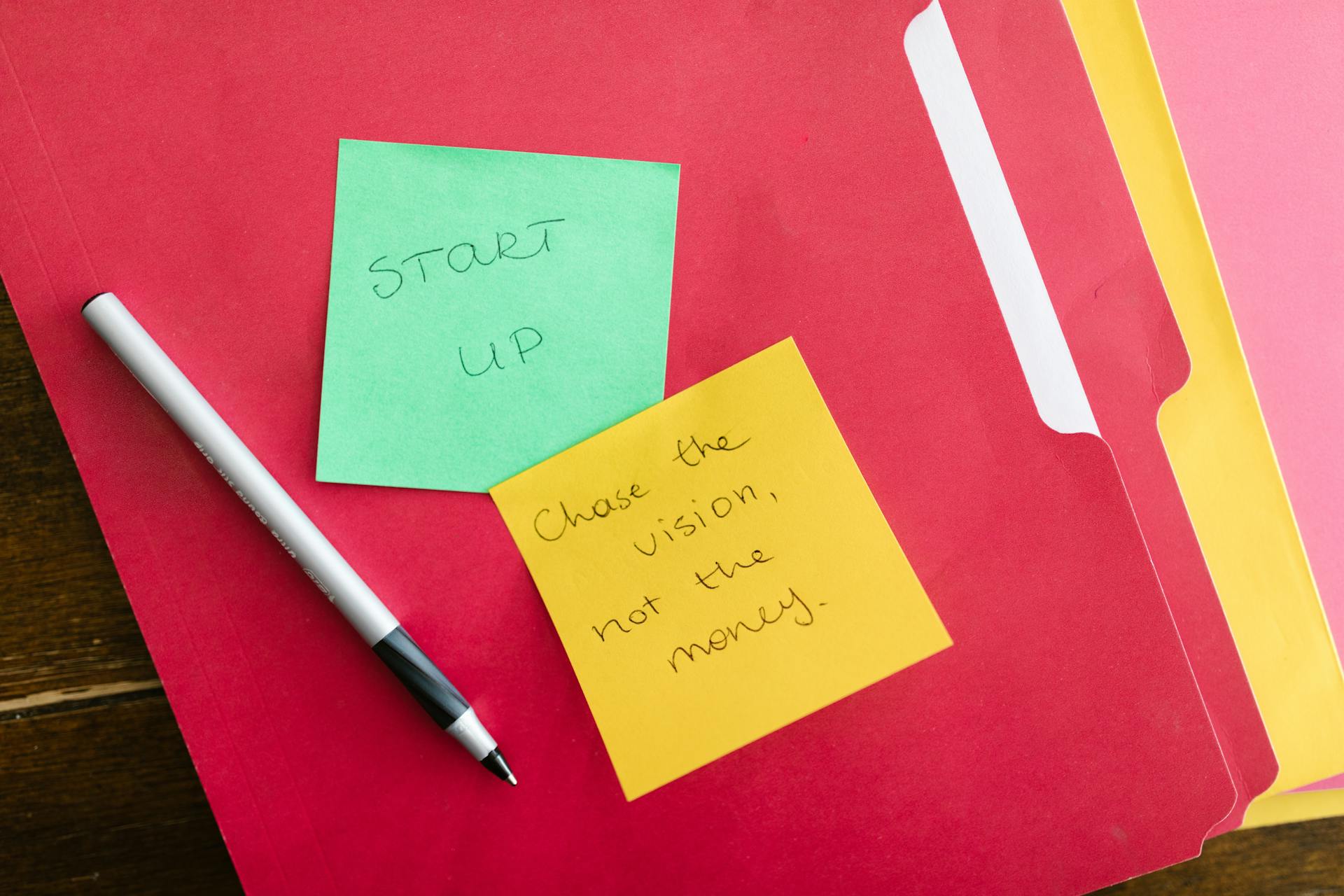 Inspiring startup quotes written on sticky notes placed on colorful folders with a pen.