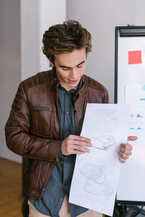 Free Adult man in casual attire presenting design sketches in a modern office. Stock Photo