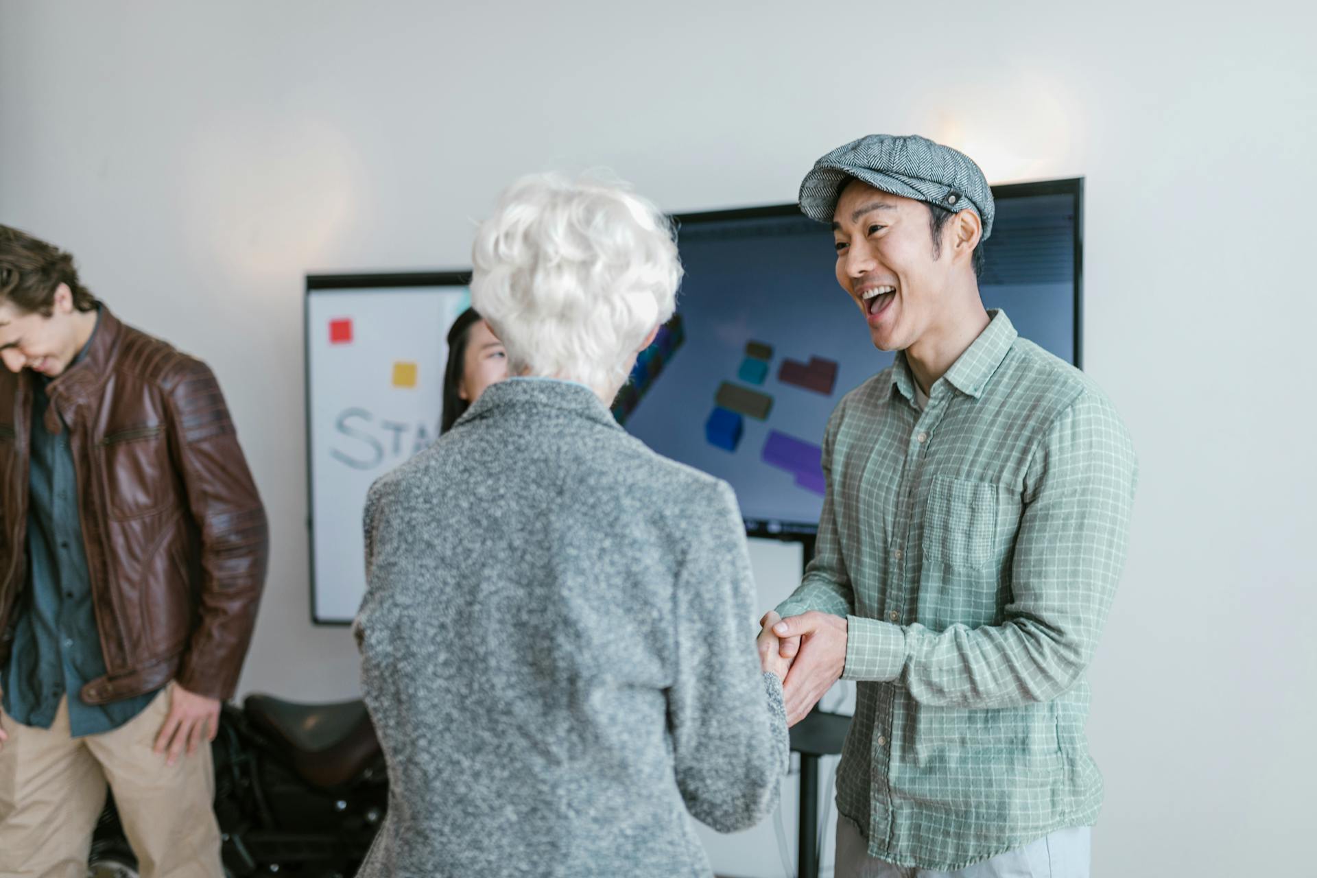 Asian man and elderly woman in a business meeting shaking hands, conveying collaboration and agreement.