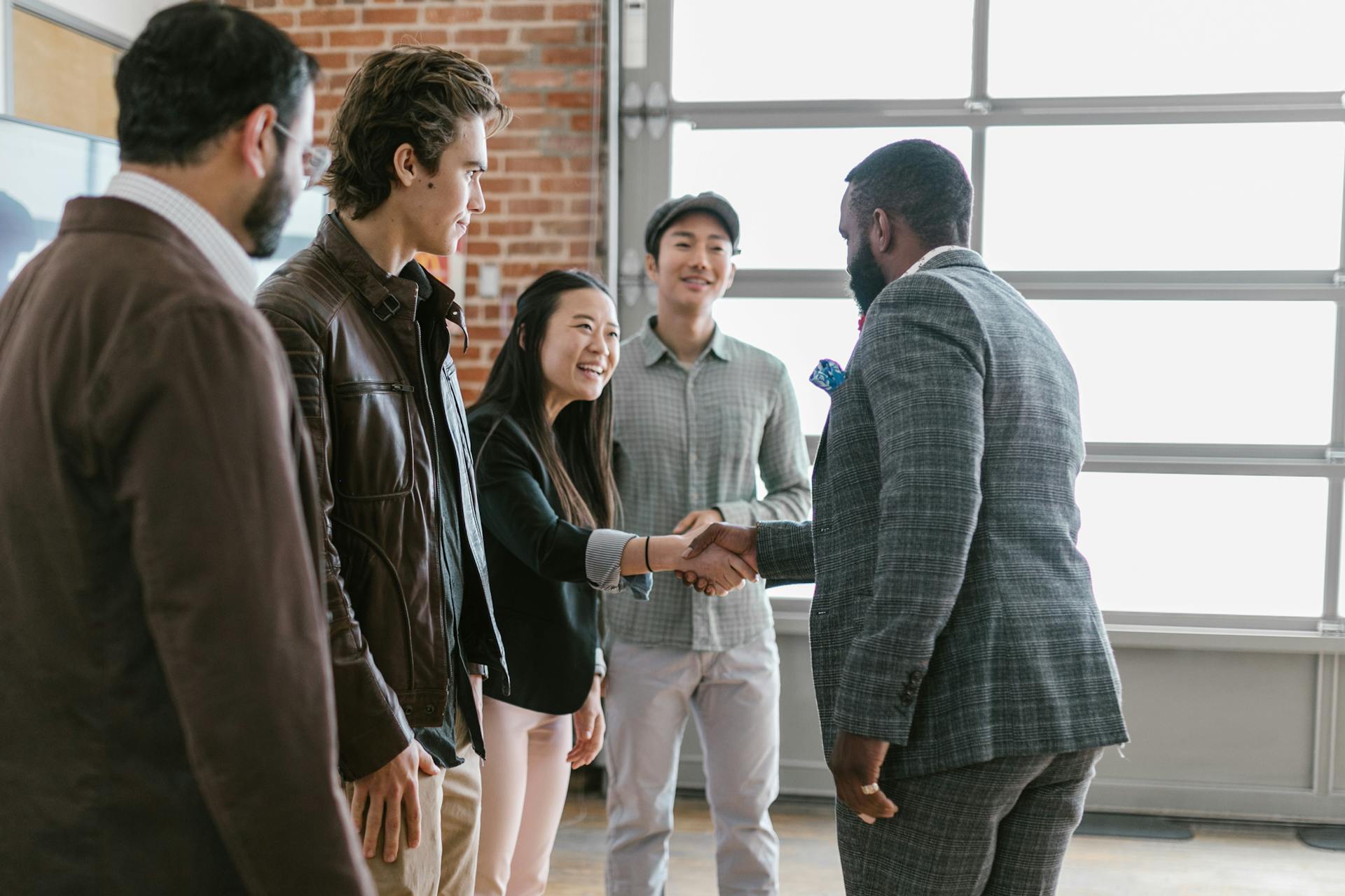 A diverse group of business professionals engaging in a handshake and discussion in a modern office space.