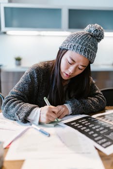 Focused young entrepreneur writing business notes in a cozy indoor setting wearing a warm beanie.
