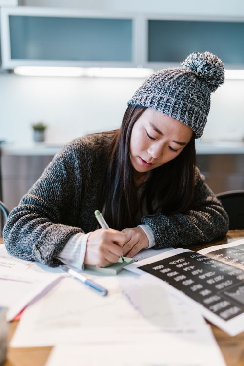 Free Focused young entrepreneur writing business notes in a cozy indoor setting wearing a warm beanie. Stock Photo