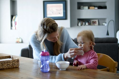 Free A nurturing woman cleans her baby's face at a kitchen table, showcasing domestic care and bonding. Stock Photo