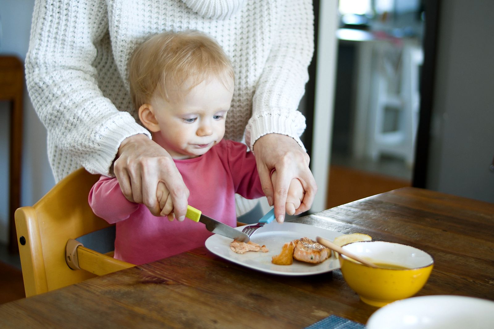 Woman helping a baby cut up food at the table — SLT paediatric feeding and dysphagia support