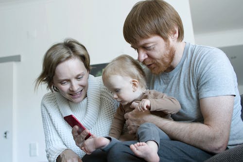 Free Couple with Their Baby Using a Cellphone Stock Photo