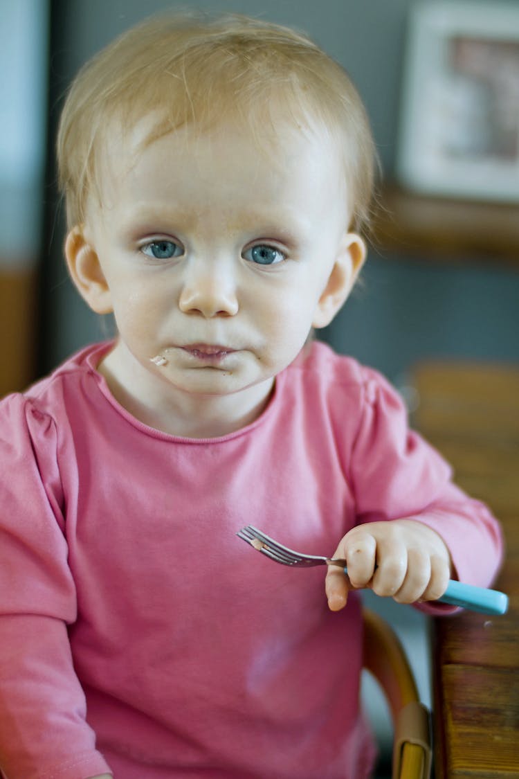 Child In Pink Crew Neck Shirt Holding A Fork