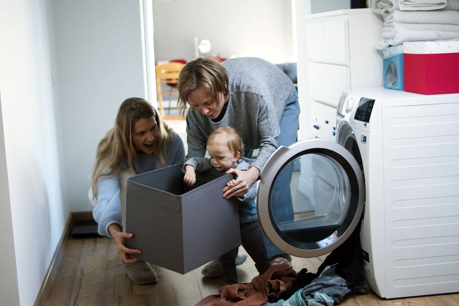 mother washing baby clothes in washing machine domestic setting