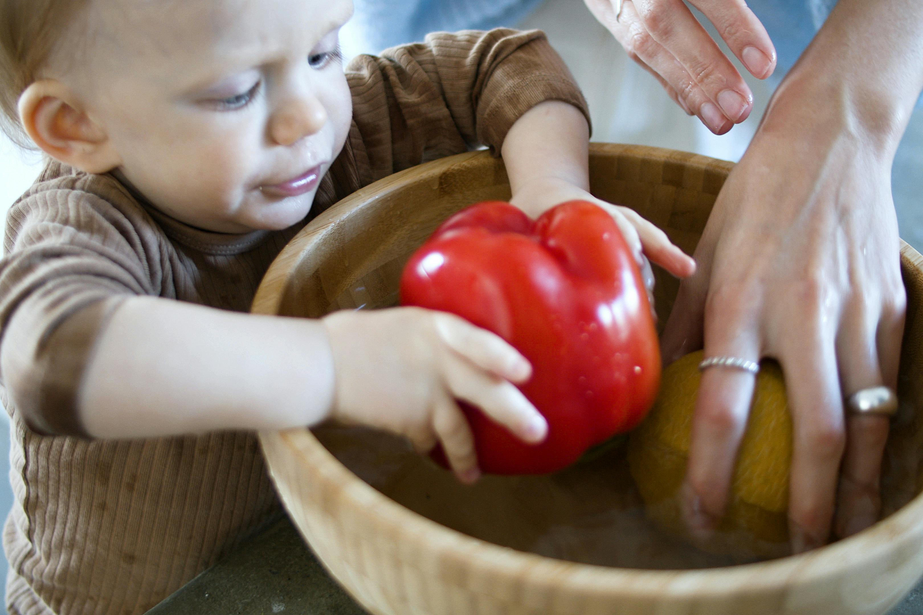 a toddler putting red pepper in wooden bowl