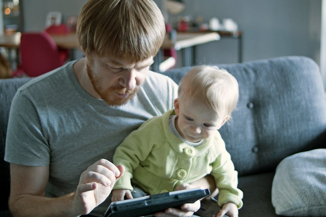 Free A Man and His Child Sitting on the Couch While Using Digital Tablet Stock Photo
