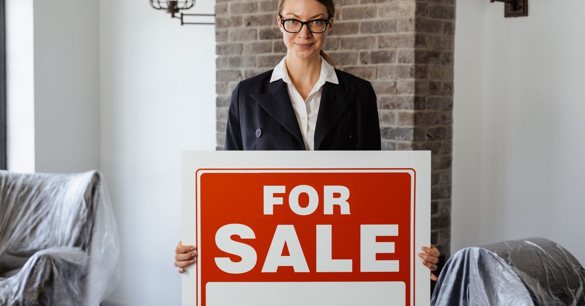 Professional real estate agent holding a 'For Sale' sign inside a modern interior.