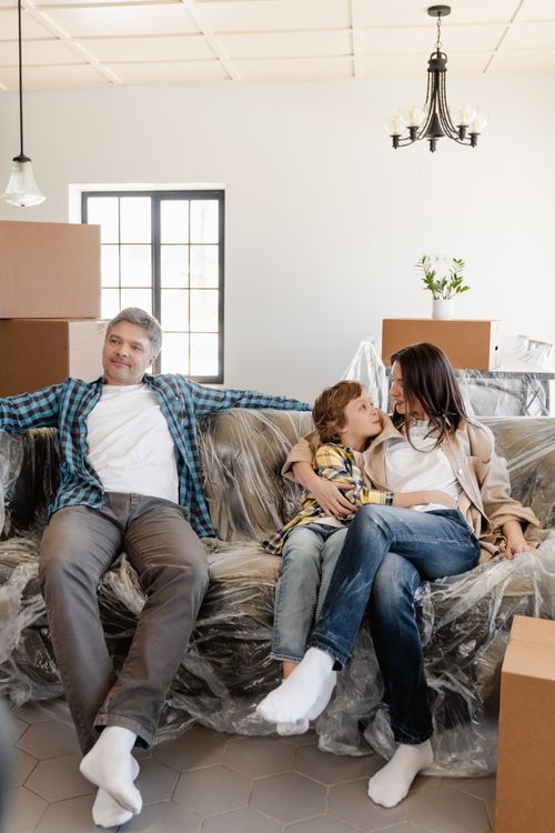 Free Family enjoying a moment together on a couch covered in plastic amid moving boxes. Stock Photo