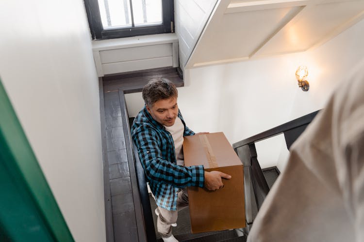 A Man Carrying A Box Upstairs