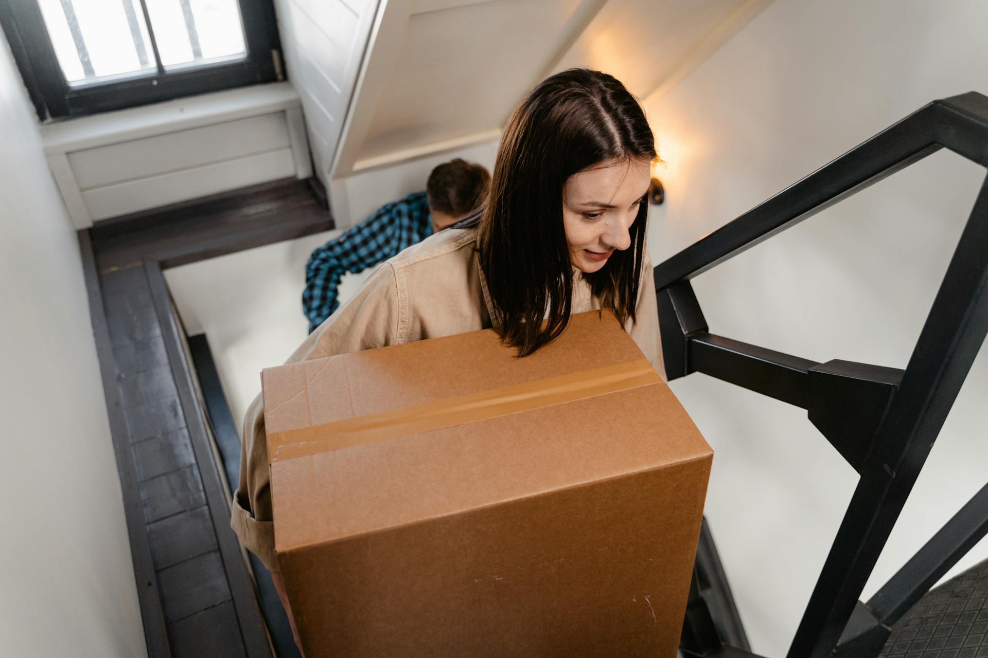 A couple carrying a large box up a staircase, symbolizing moving into a new home.