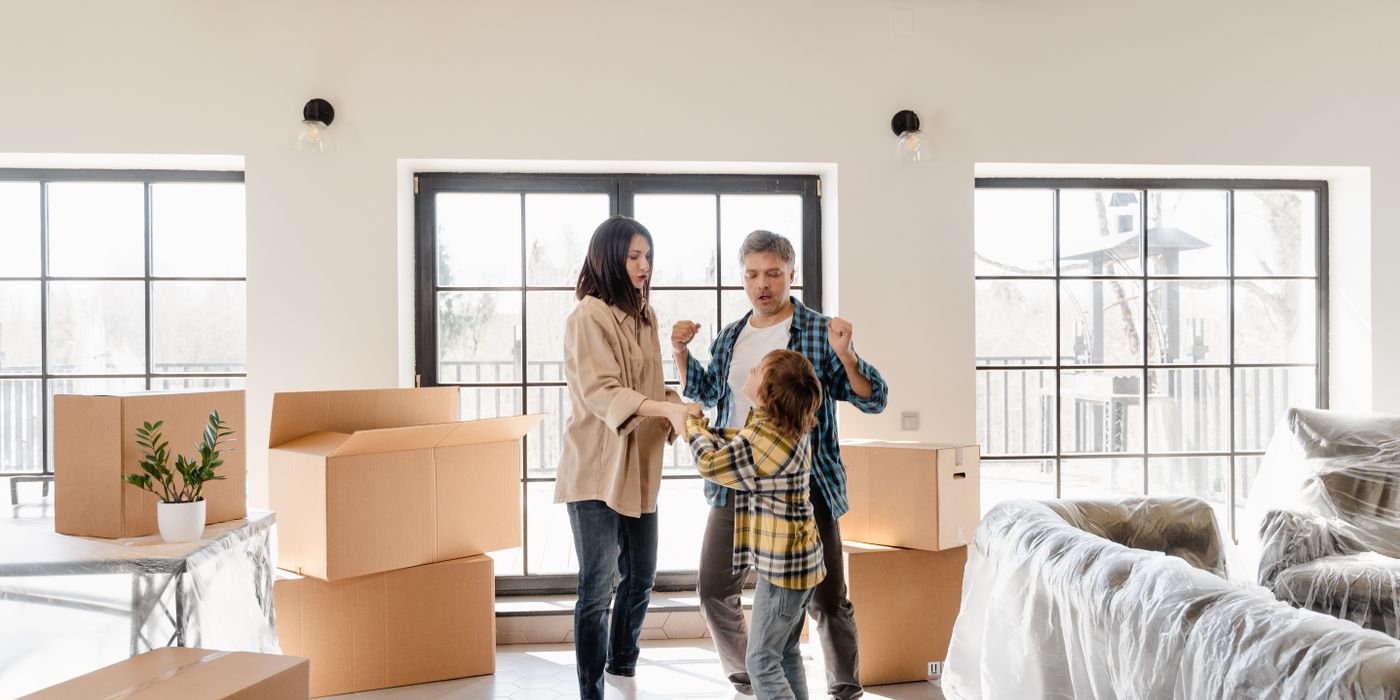 Family joyfully celebrating their new home among moving boxes and furniture.
