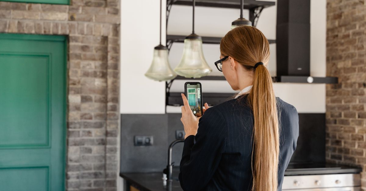 Rear view of a woman with long hair taking a photo with a smartphone in a stylish kitchen.