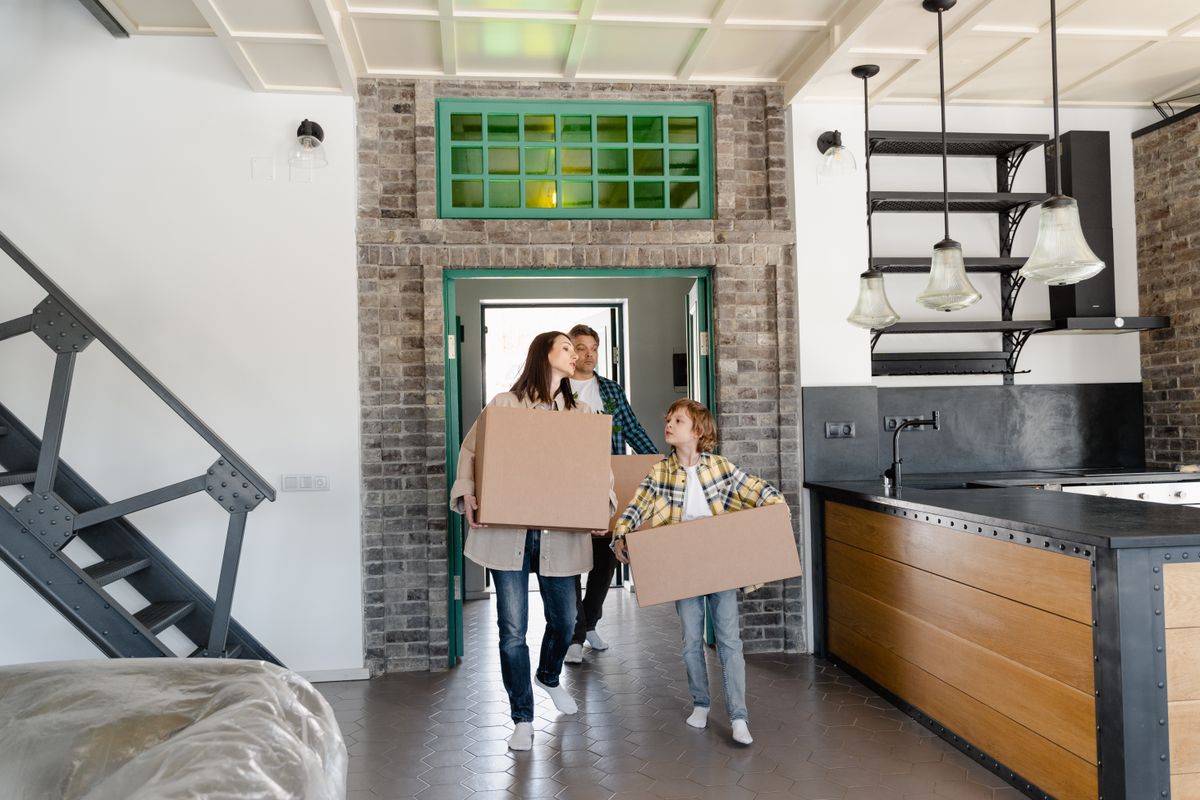 A family carrying cardboard moving boxes into a new home